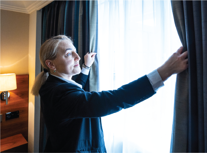 Woman draws curtains open in bright room.